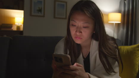 close up of woman spending evening at home sitting on sofa with mobile phone scrolling through internet or social media 4