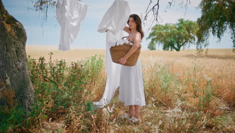 country lady taking linen from rope at summer field. woman put laundry to basket