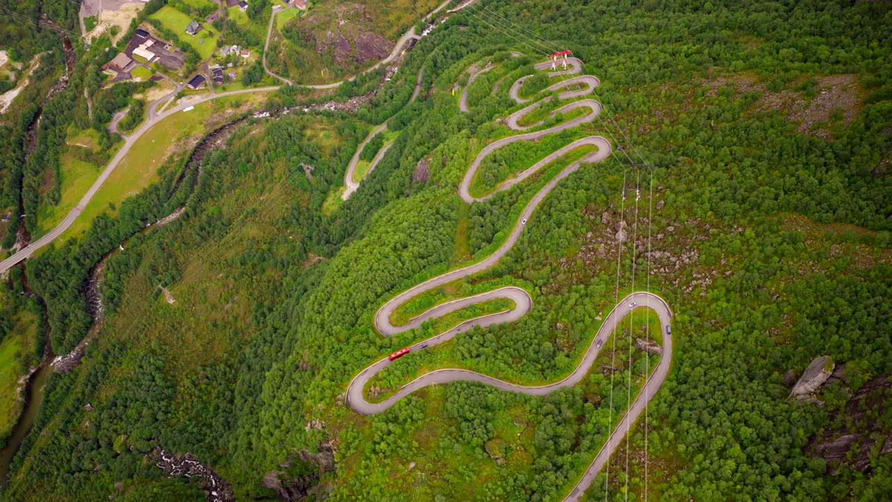 Famous winding hairpin road descending steep green mountain slope in summer in Norway. Aerial top-down backward
