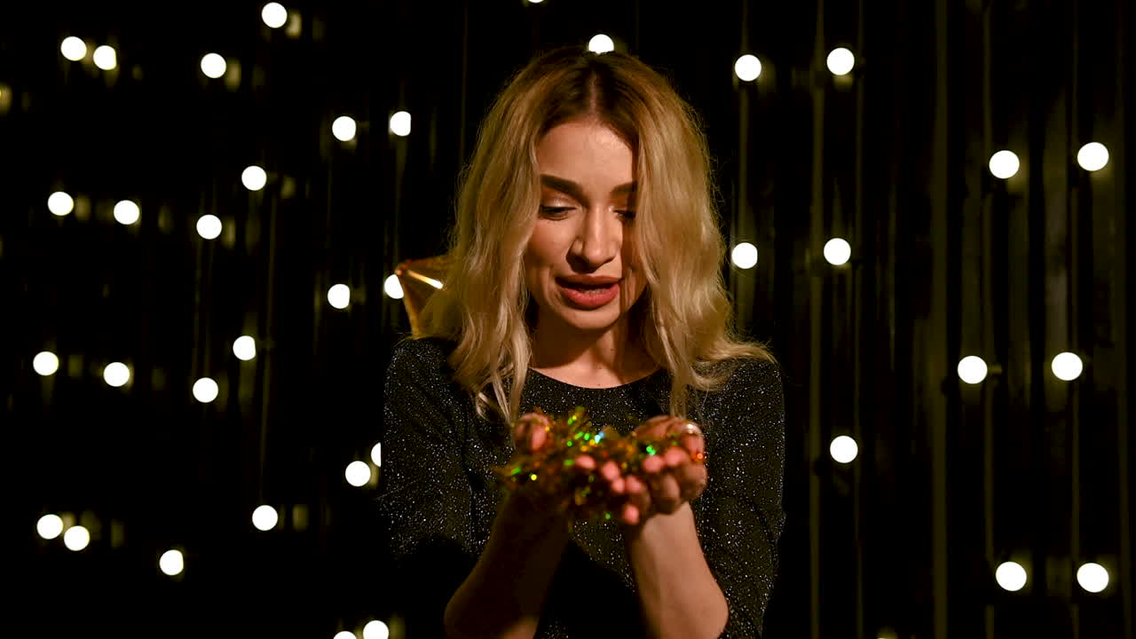 mujer bonita joven que sopla confeti de brillo dorado