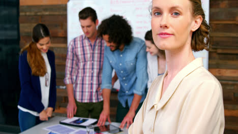 Woman-standing-with-arms-crossed-while-colleague-discussing-in-background