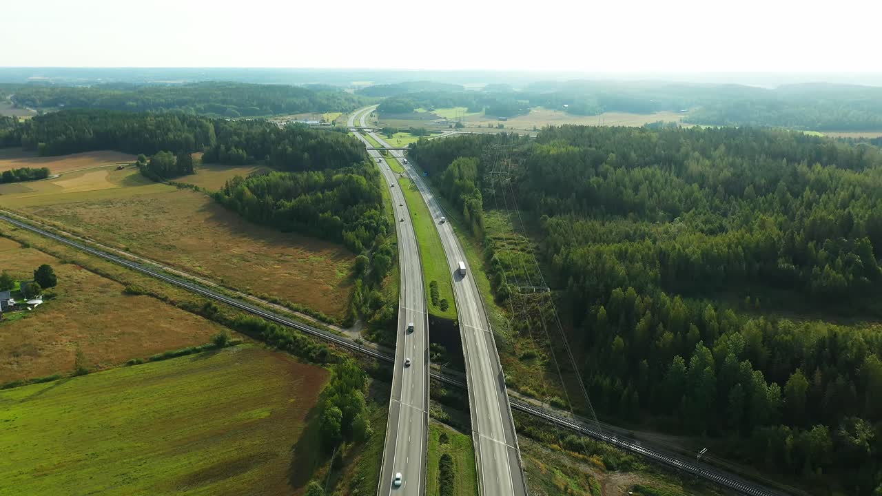 Widok lotniczy 4K w ruchu do przodu czteropasmowej autostrady z samochodami i ciężarówkami jadącymi w obu kierunkach w zamglonym letnim porannym słońcu