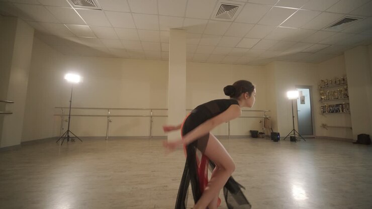 Un gruppo di giovani allievi di danza classica in abbigliamento da ballo nero che eseguono esercizi in un ampio studio di danza con pavimenti in legno e barre a muro. Espressioni concentrate e movimenti sincronizzati