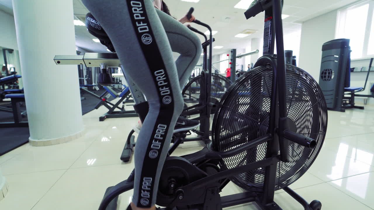 Fit young sexy women in sportswear using indoor bikes at the gym. Strong female athletes are doing cardio workout on cycles at health club.