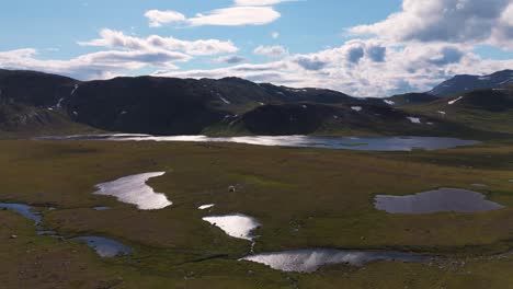 aerial view of a serene landscape featuring lush greenery, tranquil lakes and majestic mountains under a partly cloudy sky