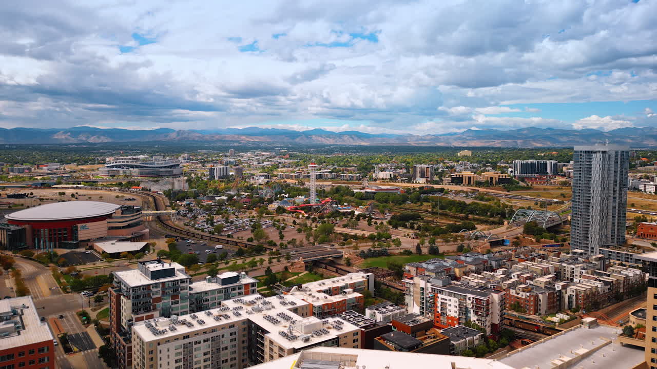 Denver, USA, 28 July 2025: Vast panorama of Denver, Colorado, USA. Amusement park with observation tower in center. Cloudy sky and mountain range at backdrop. Aerial view