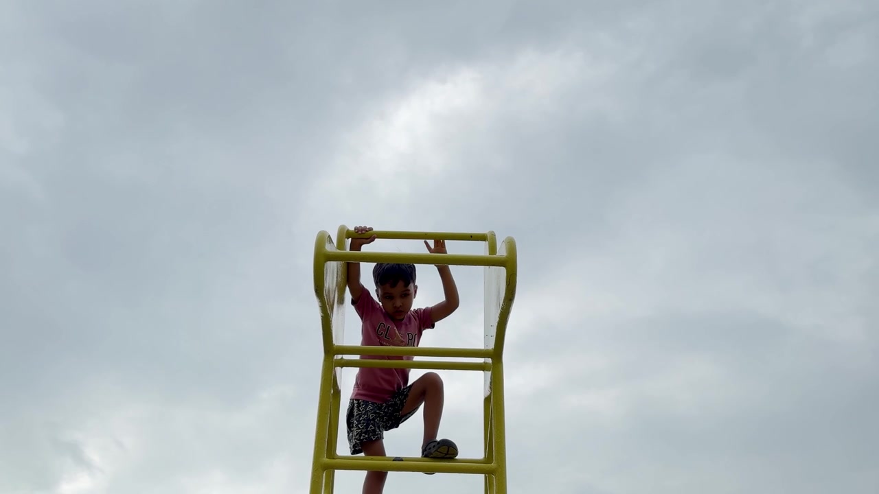 Little Boy Playing On Outdoor Playground Equipment Under Overcast Sky
