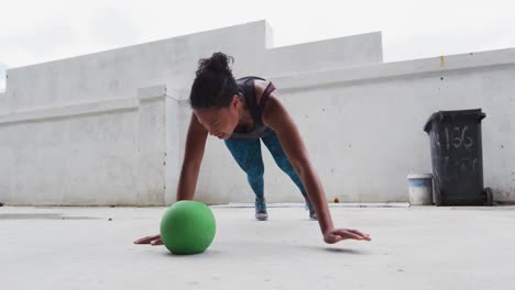 mujer afroamericana haciendo ejercicios de flexión en una pelota de medicina en un edificio urbano vacío
