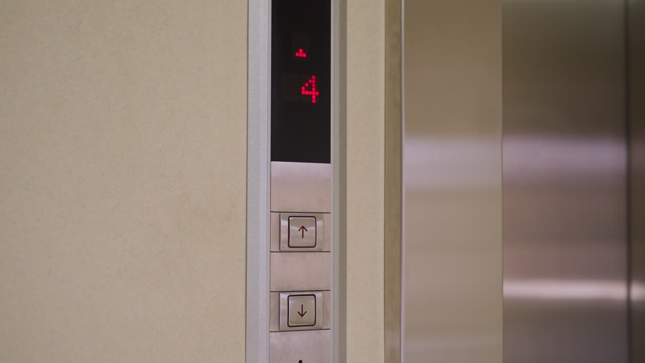 Elevator control panel showing floor 3 with red digits, up and down arrows, and modern design. Smooth, polished metallic finish reflecting elevator functionality and office environment