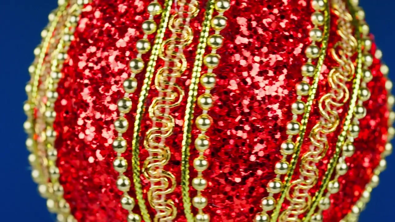 Ornamento natalizio rosso scintillante con perline dorate che ruota su sfondo blu