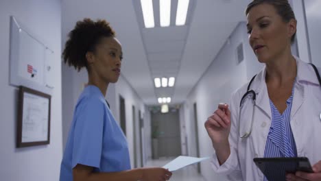 diverse female doctor and medical worker talking walking in hospital corridor