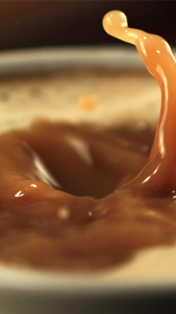 Gros plan au ralenti de gouttes de café éclaboussant une boisson crémeuse