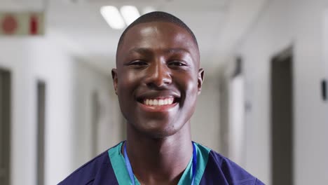 Video-portrait-of-smiling-african-american-male-medical-worker-standing-in-hospital-corridor