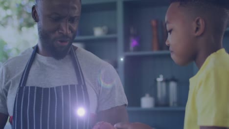 Animation-of-lights-over-happy-african-american-father-and-son-cooking-together