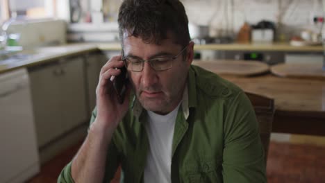 caucasian man sitting at table, using smartphone, talking at home