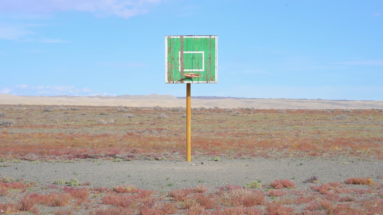 A weathered basketball hoop, a powerful metaphor for distant athletic dreams and aspirations, stands abandoned and forgotten in the vast emptiness of the remote and silent Mongolian plains