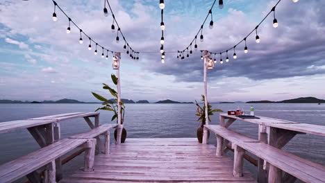 white wooden pier with benches by the sea decorated with chain lights