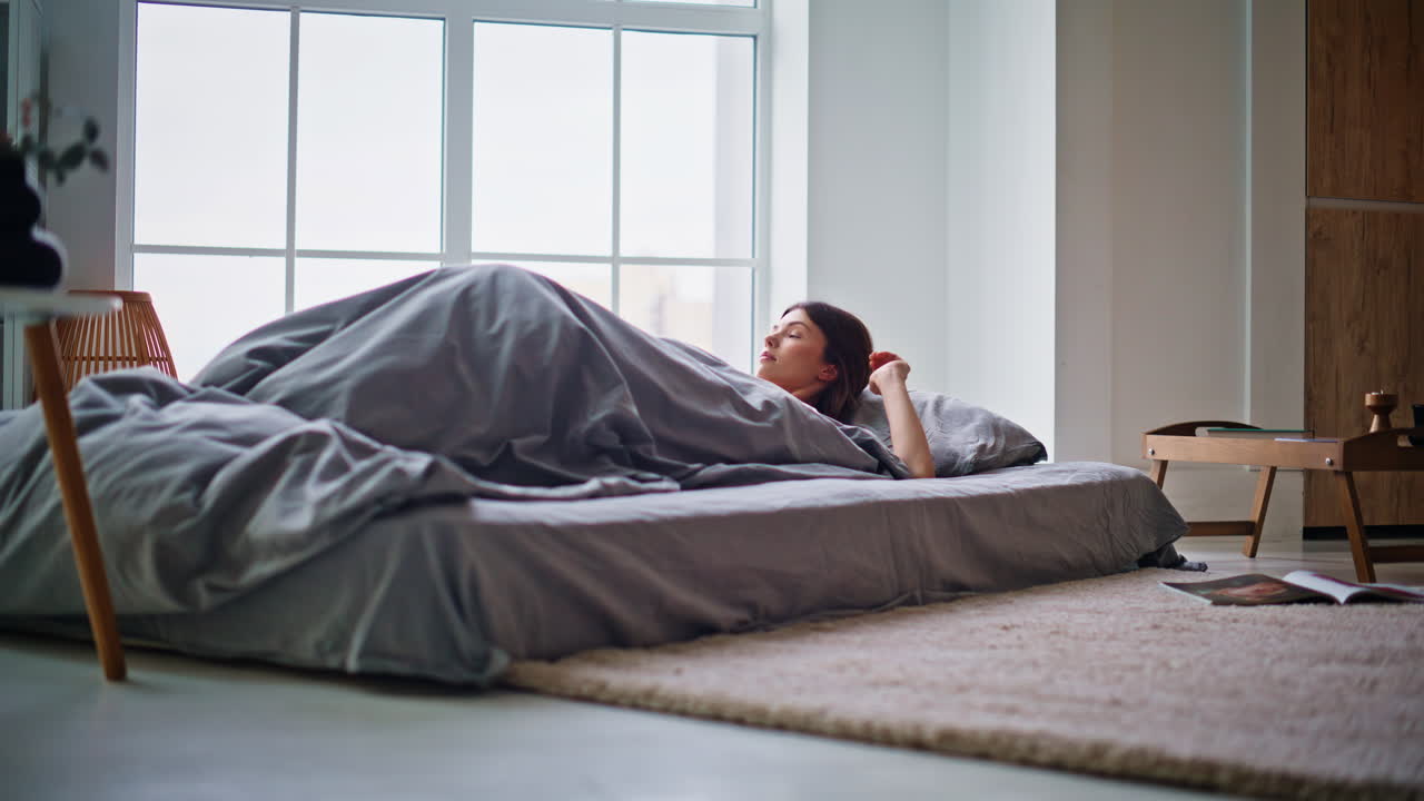 Ung brunette sover på madras. Glad kvinde starter ny dag med at strække arme