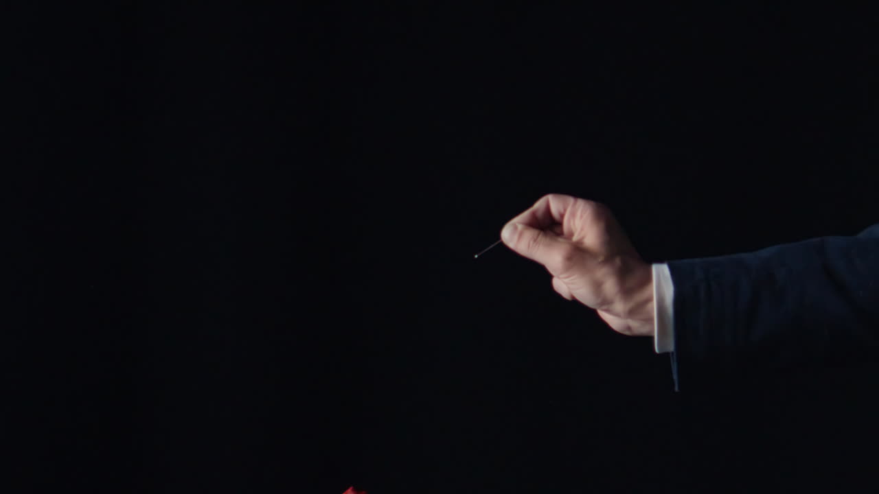 Primo piano di una mano che fa scoppiare un palloncino rosso con uno spillo su sfondo nero. Buon compleanno