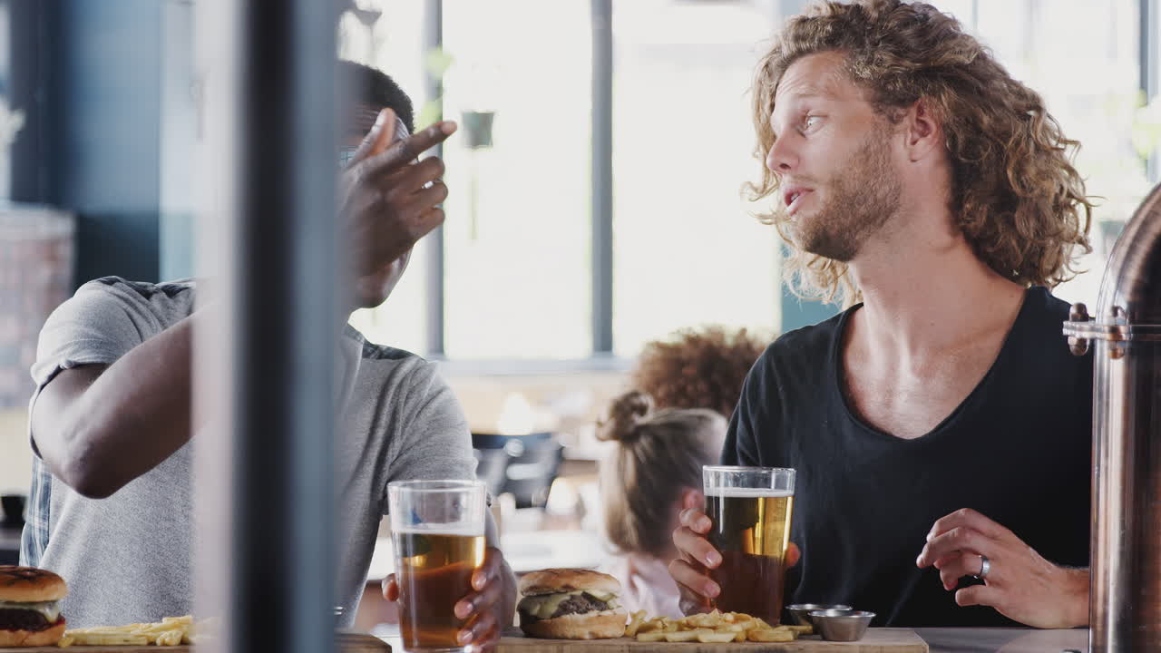 Two Male Friends Eating Food And Drinking Beer In Sports Bar