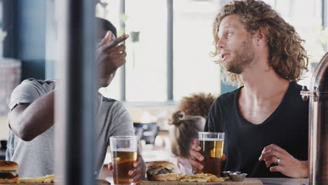 dos amigos hombres comiendo comida y bebiendo cerveza en un bar deportivo