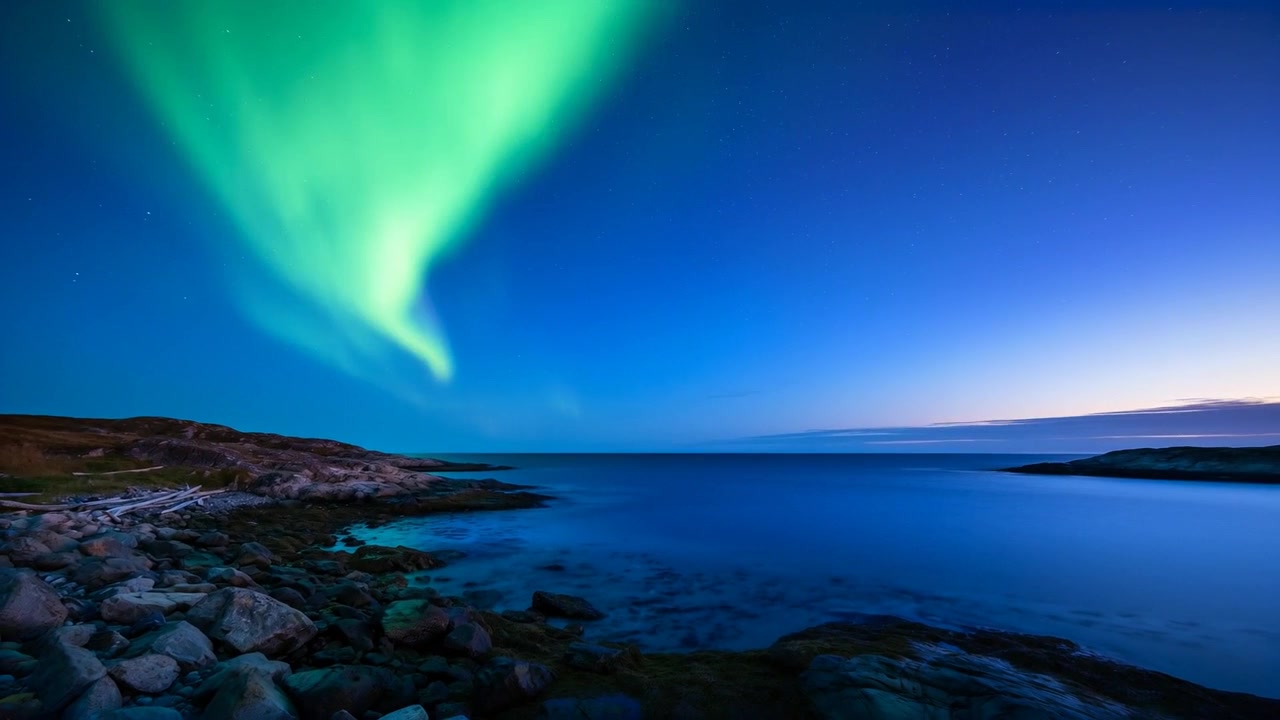 Aurora a spirale luminosa che appare, si estende a sinistra su una costa rocciosa al crepuscolo, riflettendosi sul mare