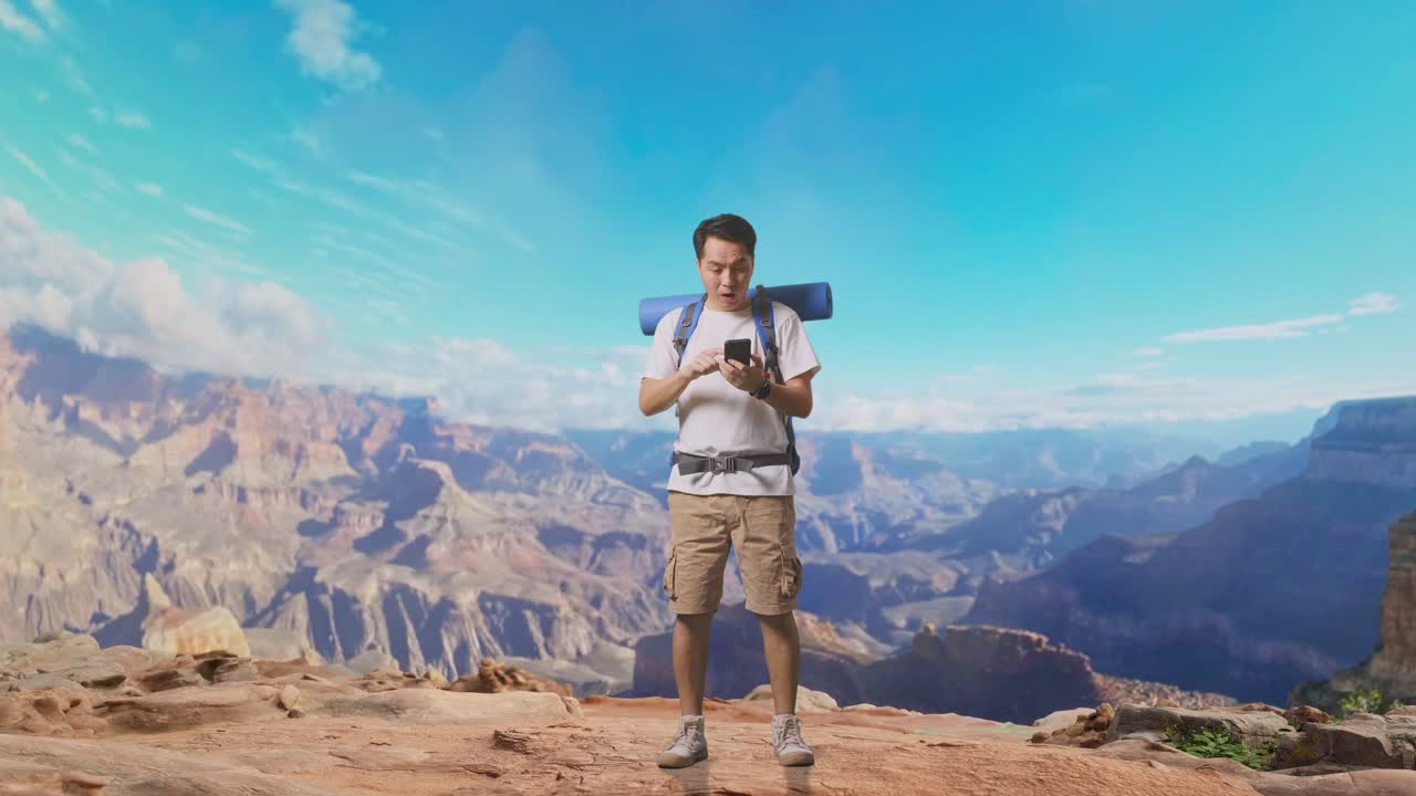Full Body Of Asian Male Hiker With Mountaineering Backpack Looking At The Smartphone And Saying Wow While Traveling At The Top Of Mountain