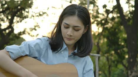 young attractive asian woman playing acoustic guitar in a summer park. woman with happy emotion concept. slow motion.