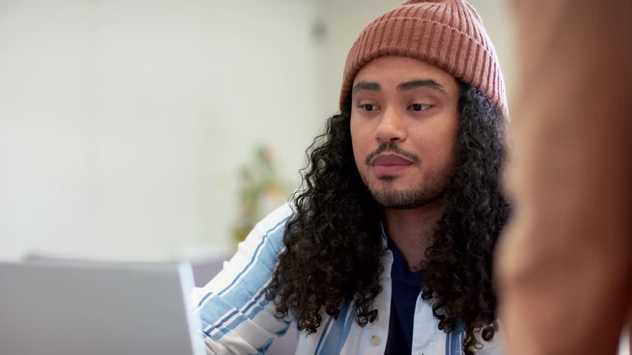 Colega falando, homem digitando no laptop e explicando enquanto checa o smartwatch em casa