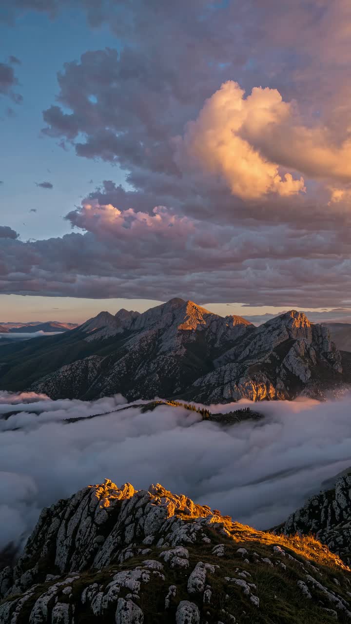 Aerial video captures a dramatic mountain landscape at sunset, with vibrant clouds and misty