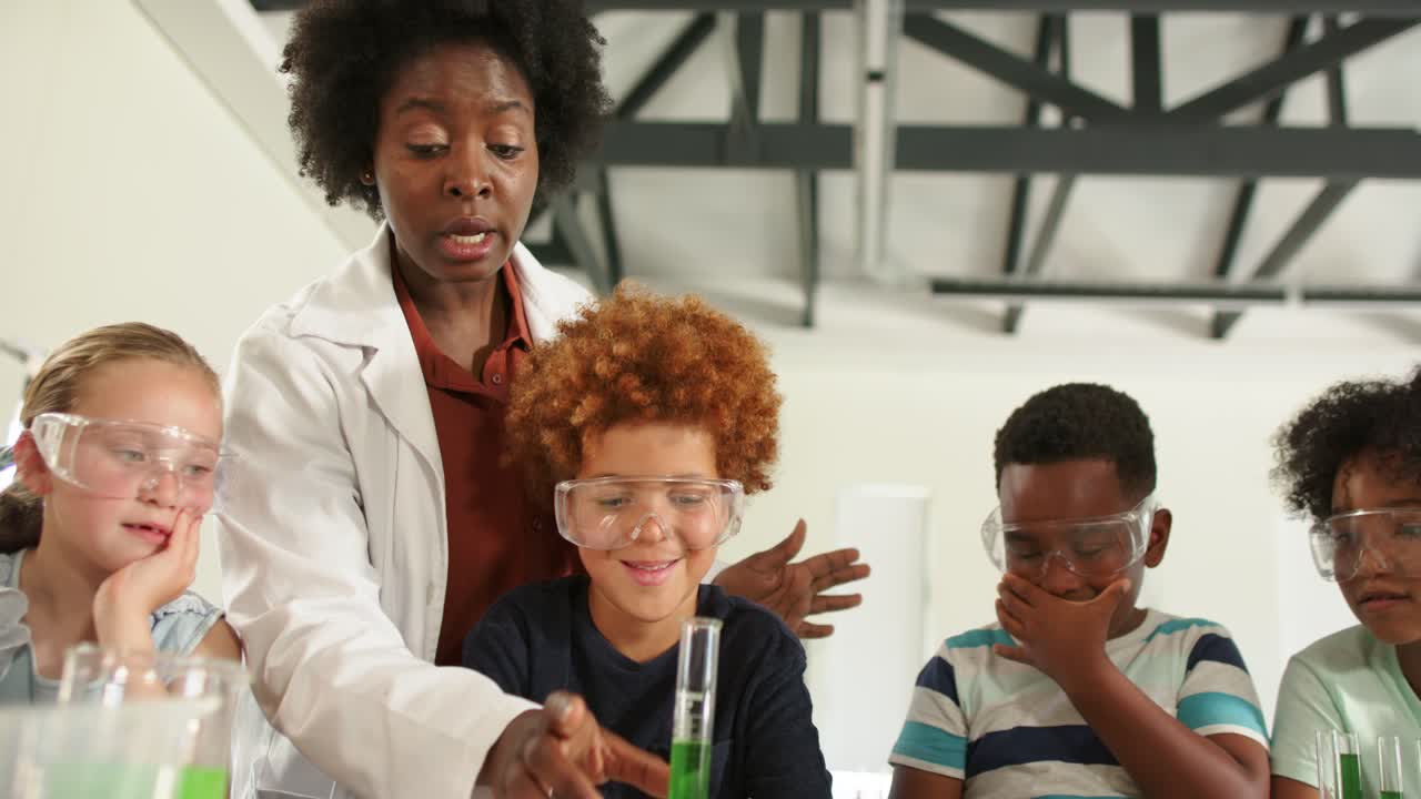 Insegnante afroamericano che spiega una dimostrazione di laboratorio a dei bambini, mentre si sporge in avanti e indica un cilindro graduato