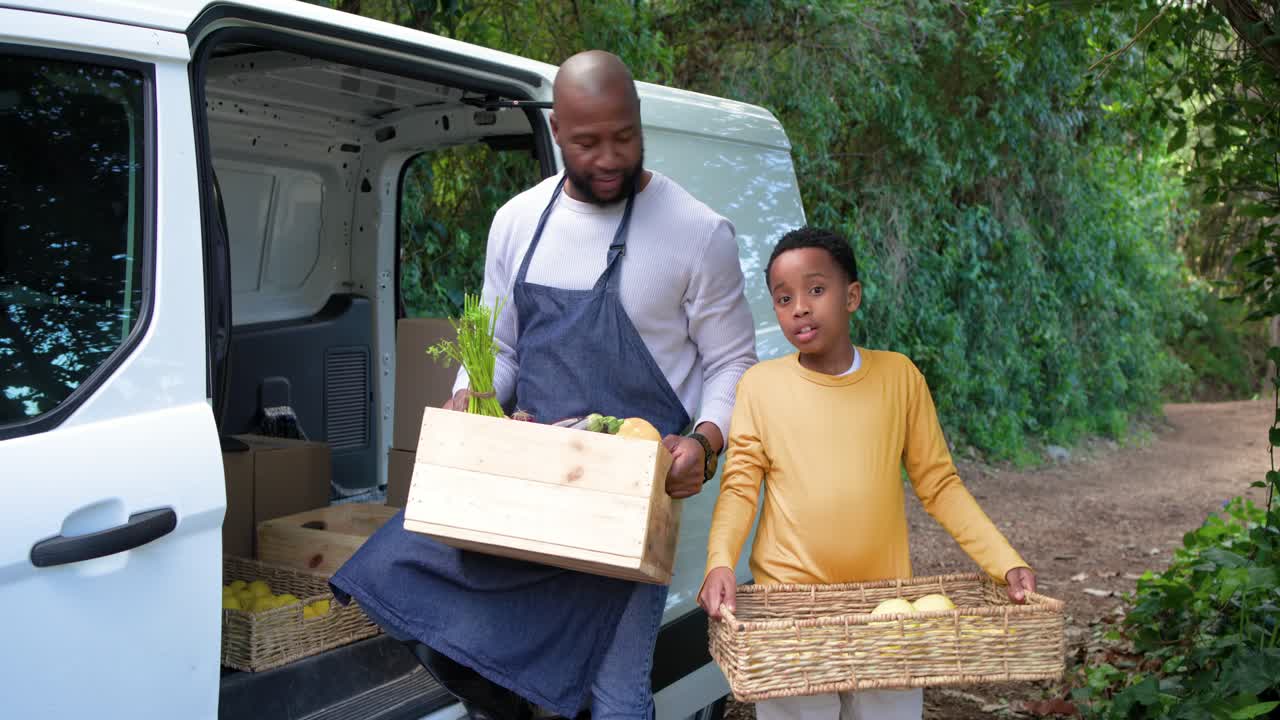 Pai e filho afro-americanos carregando engradado e cesta, entregando produtos em bosque ao chegar na van
