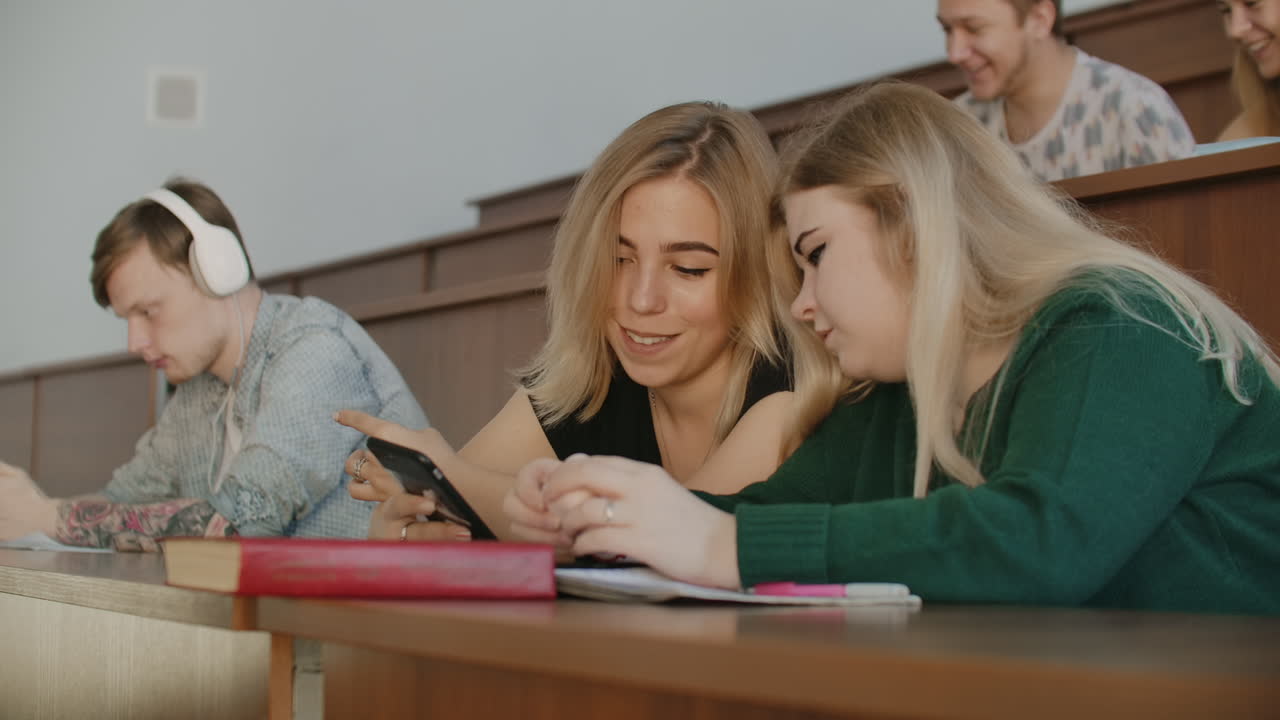 Cheerful students are using smartphones and chatting during break between lectures at university. Modern technology. Cheerful students multiethnic group are