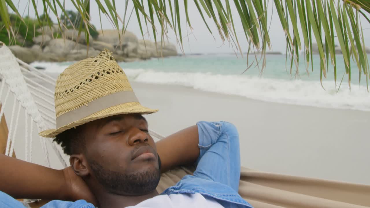 High angle view of African american man sleeping in a hammock on the beach 4k