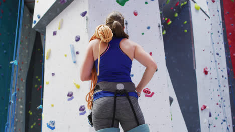 Vista-Trasera-De-Una-Mujer-Caucásica-Con-Una-Cuerda-Sobre-Su-Hombro-En-Un-Muro-De-Escalada-Interior.