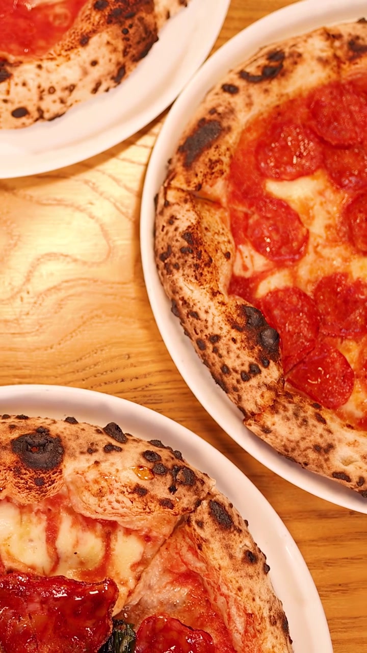 Ovenfra panorerer kameraet hen over håndlavede pepperoni pizzaer og italienske forretter på et varmt træbord.