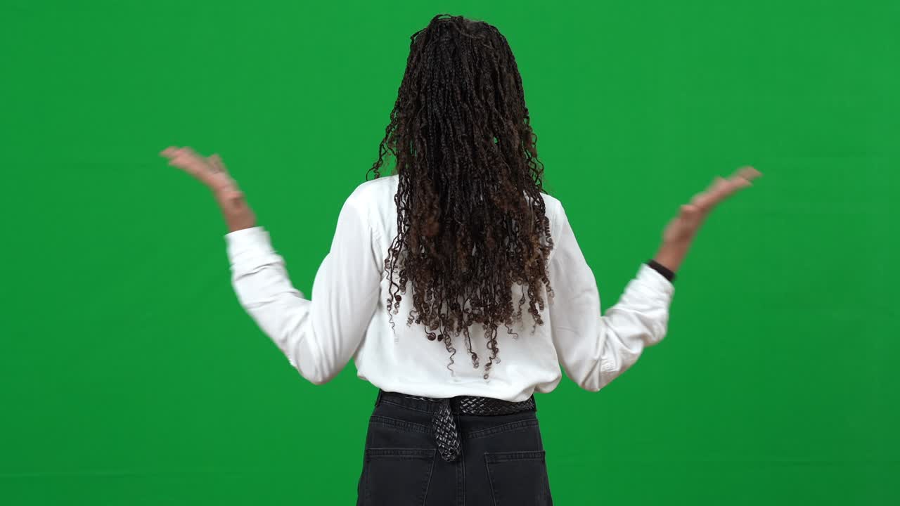 Back view of joyful teen African American girl pointing around on chromakey making excited gesture. Teenage gamer playing online in futuristic reality on green screen. Gaming and adolescence.