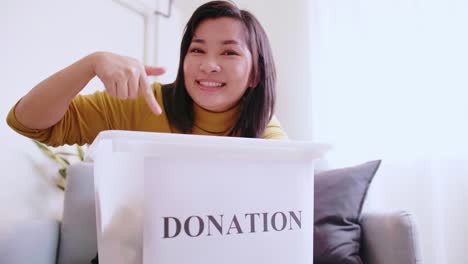 Lovely-woman-pointing-to-box-with-donations,-inviting-others-to-donate-too