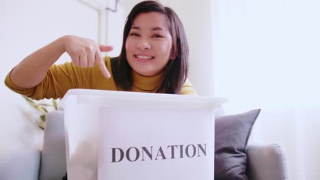 lovely woman pointing to box with donations, inviting others to donate too