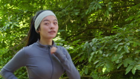 Side-View-Of-Young-Woman-Exercising-Running-Through-City-Park-Wearing-Wireless-Earbuds