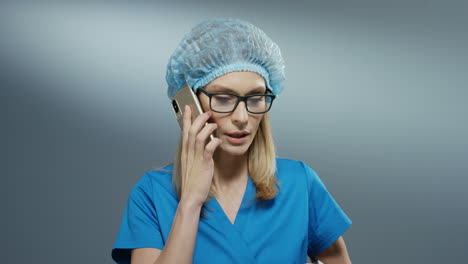 Joven-Asan-Doctora-Rubia-Ocupada-Con-Traje-Azul,-Sombrero-Y-Gafas-Hablando-Por-Teléfono-Emocionalmente