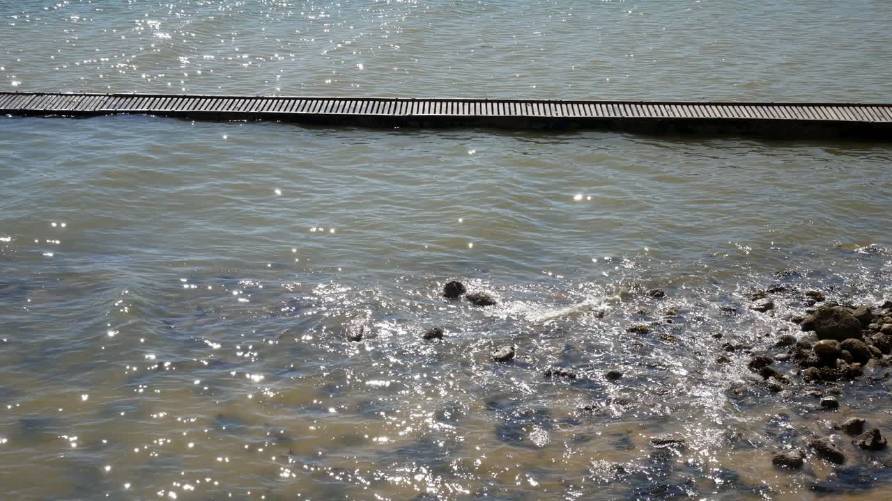 바위 해안선을 씻는 반짝이는 파도의 표면에 나무 해변 판자