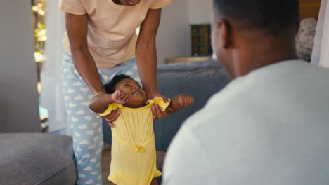 family shot as parents wearing pyjamas play with young daughter indoors at home