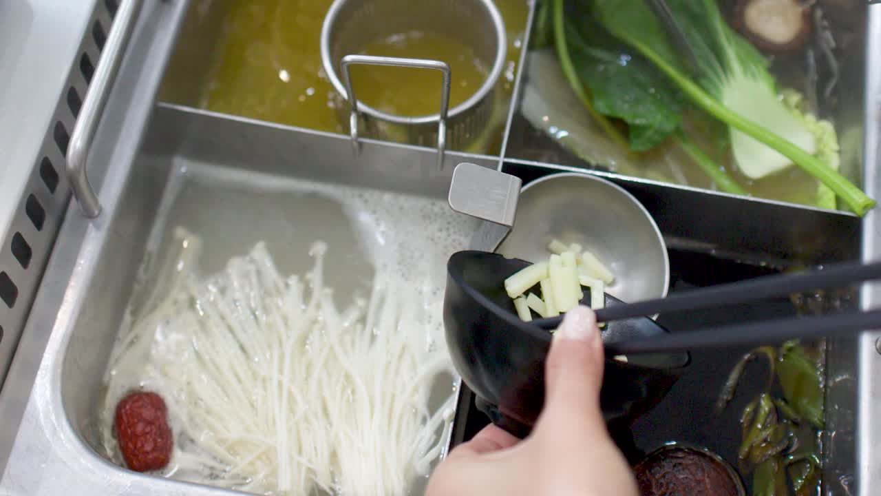 様々な野菜が入った沸騰した鍋に、箸を使って具材を加える人