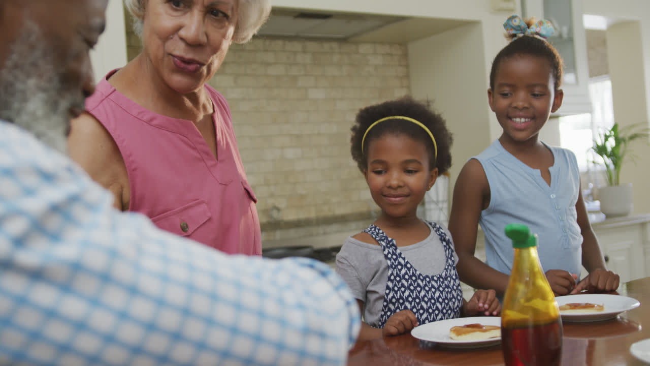 Happy african american grandparents with granddaughters having breakfast and talking