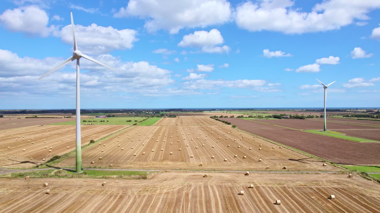 The aerial footage reveals a picturesque sight—a row of wind turbines spinning gracefully within a Lincolnshire farmer's newly harvested field, where golden hay bales add rustic charm