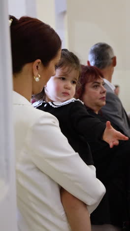 a woman holds a young child during a religious gathering, with people in the background