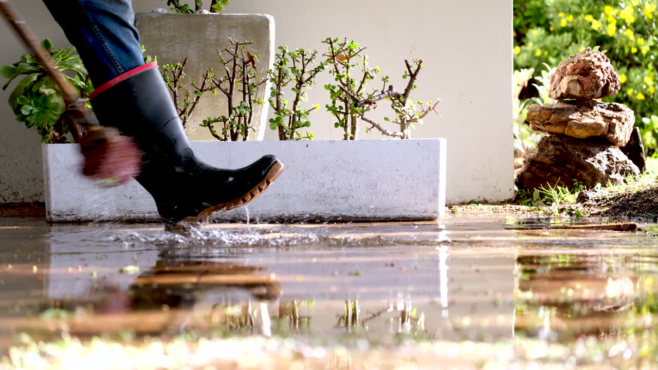 Side view of man sweeping stagnant rainwater from driveway after rainstorm