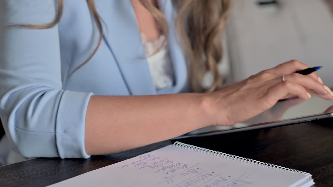 Donna con blazer blu che lavora su un tablet e scrive su un quaderno a una scrivania in ufficio