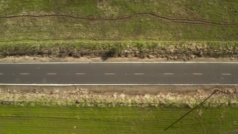 Toma-Cenital-De-La-Carretera-Que-Conduce-A-Verdes-Colinas-Con-Cielo-Azul-Y-Nubes-Blancas-Y-árboles-En-La-Carretera-Rural